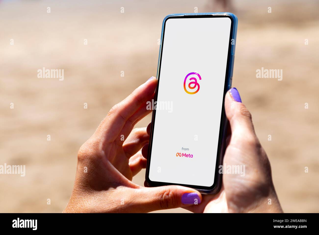 Threads app opening in a smartphone screen. Woman in the beach with a mobile phone in her hands. Text-based conversation application. Social network Stock Photo