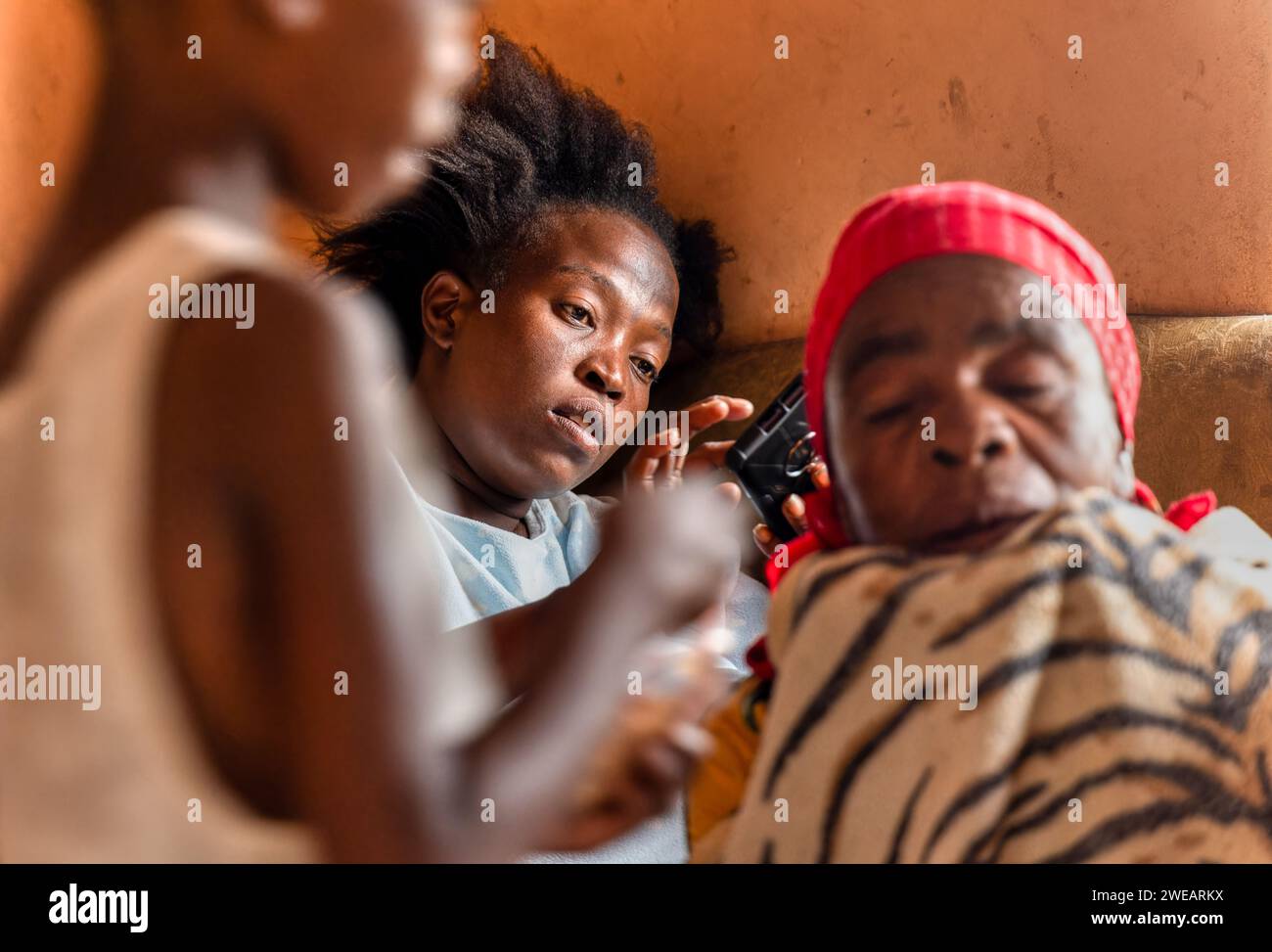village african woman , using the phone, sited on the couch with a granny and a kid Stock Photo
