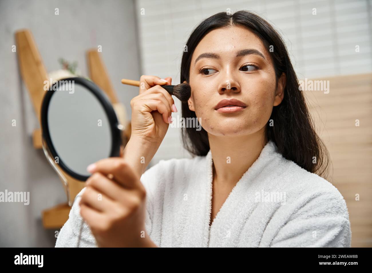 young asian woman with hair and acne applying powder with cosmetic brush, skin issues
