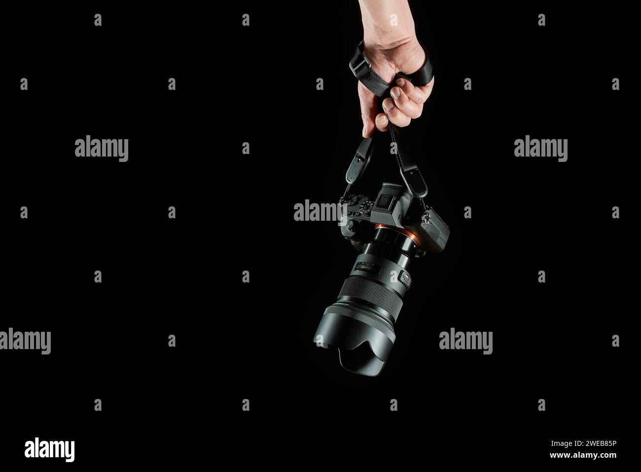 photographer holding a mirrorless camera dangling on the neck strap isolated on black background Stock Photo