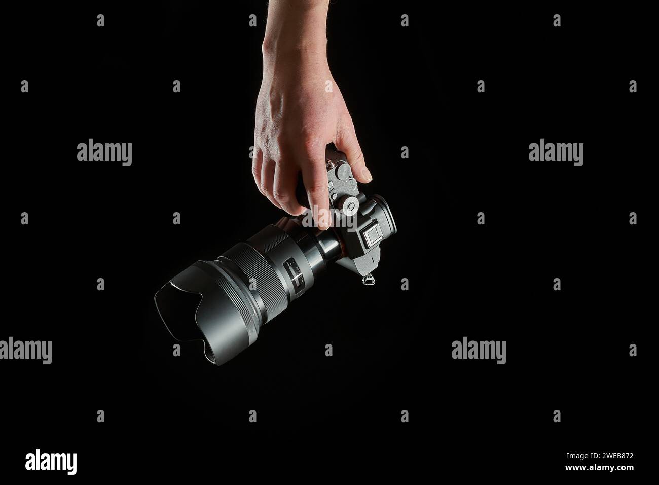 young photographer holding a mirrorless camera in his hand isolated on black background Stock Photo
