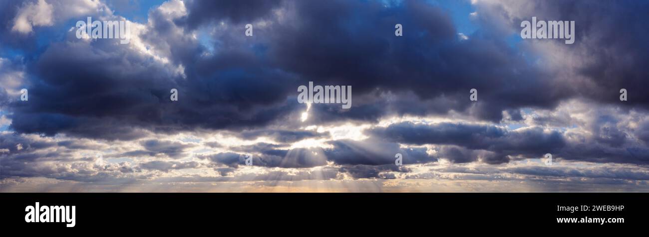 Sun rays shine through dark rainy clouds in the sky. Stock Photo