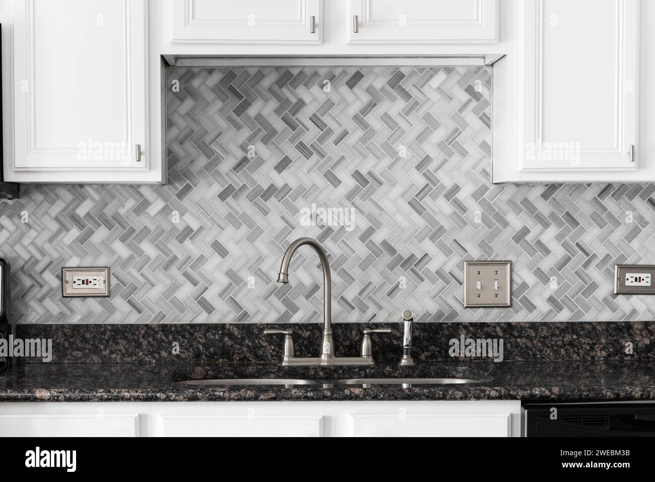 A kitchen faucet detail with white a marble herringbone tile