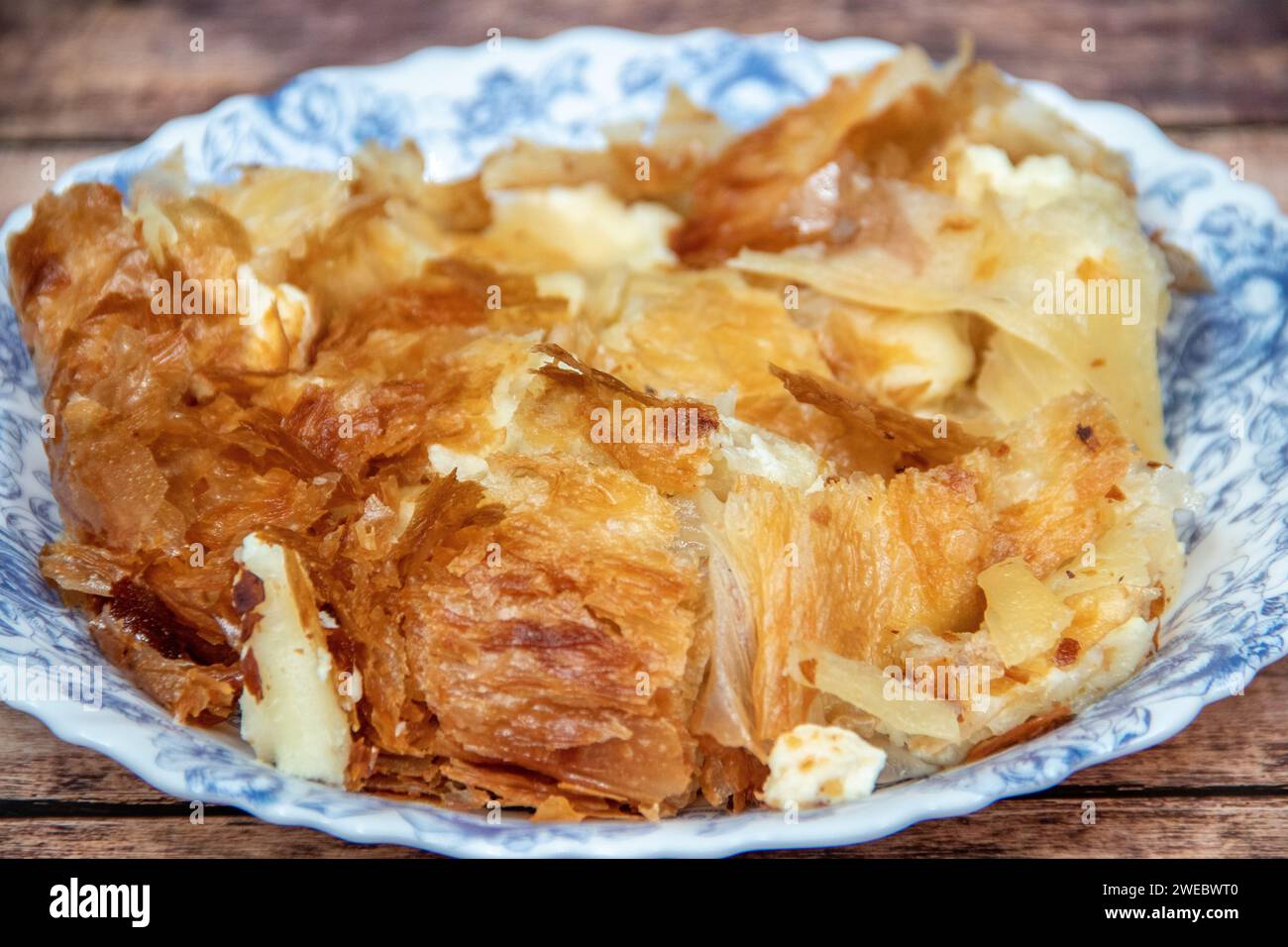 Serbian dish called Burek (cheese pie) served for breakfast at the plate with cutlery and fresh home made yogurt in cup Stock Photo