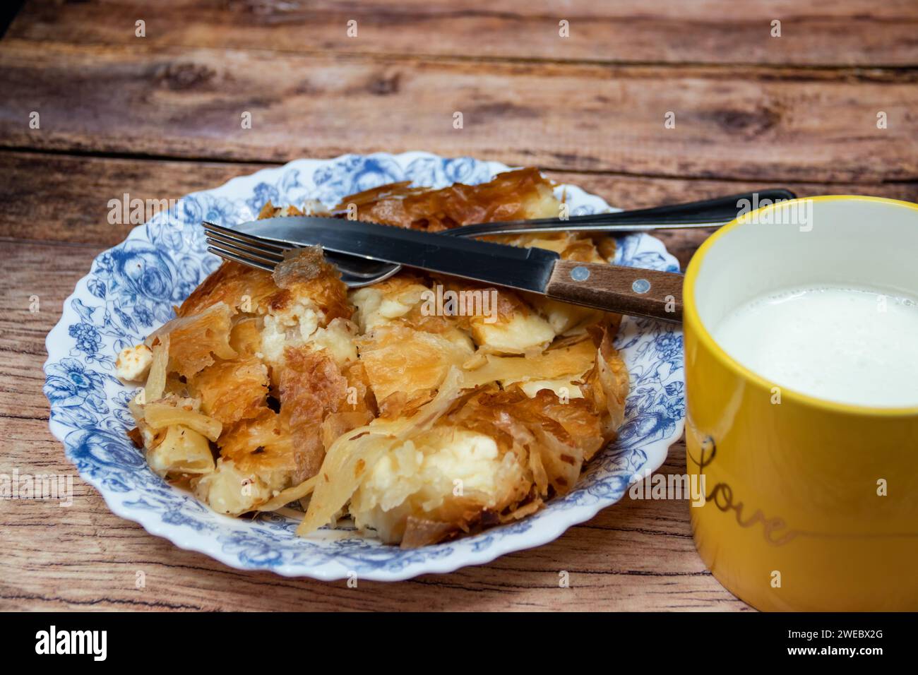 Serbian dish called Burek (cheese pie) served for breakfast at the plate with cutlery and fresh home made yogurt in cup Stock Photo