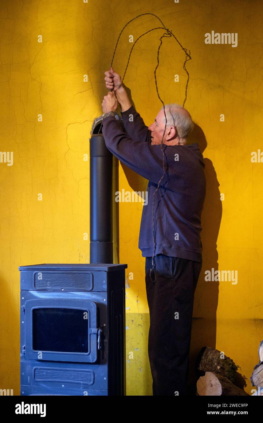 mature older male man cleaning the chimney flue using wire brush to dislodge soot on domestic home wood burner Stock Photo