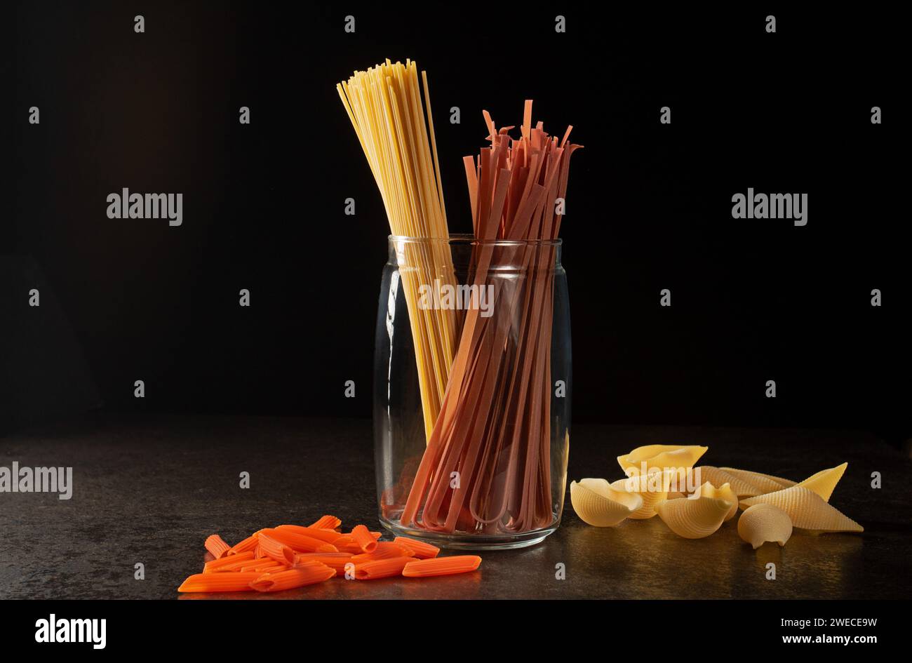 This vibrant image showcases a captivating still life arrangement of different types of italian pastas, well-lit and expertly captured against a dark Stock Photo