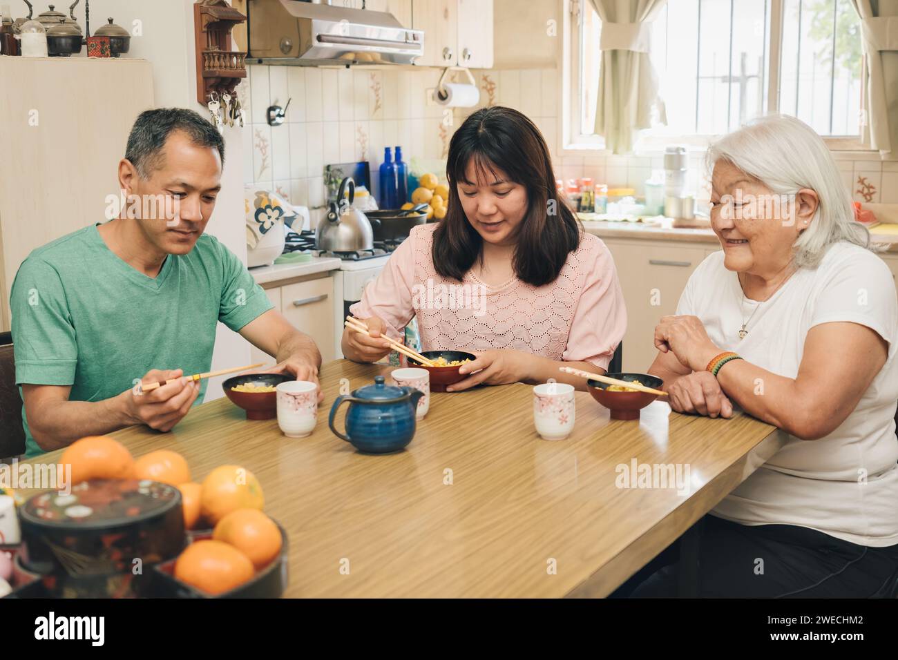 White-haired elderly mother enjoys watching her grown children sharing Japanese typical lunch Stock Photo