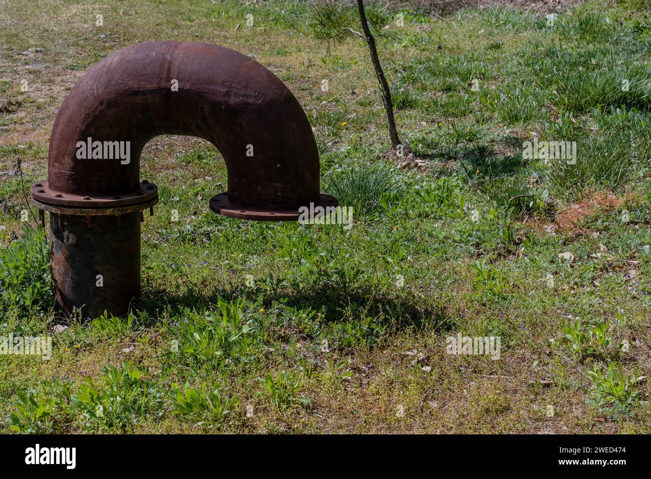 Curved iron vent pipe protruding from lush grass covered ground in wilderness Stock Photo