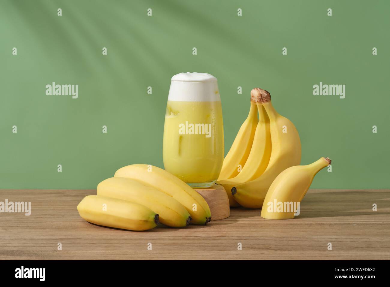 A glass of banana juice placed on a wooden podium, decorated with bunches of banana. Bananas contains an abundance of vitamin A, which restores dull s Stock Photo