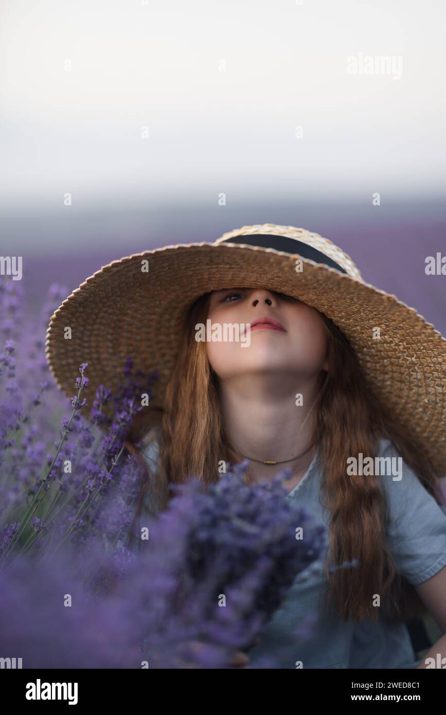 Girl lavender field in a blue dress with flowing hair in a hat stands ...