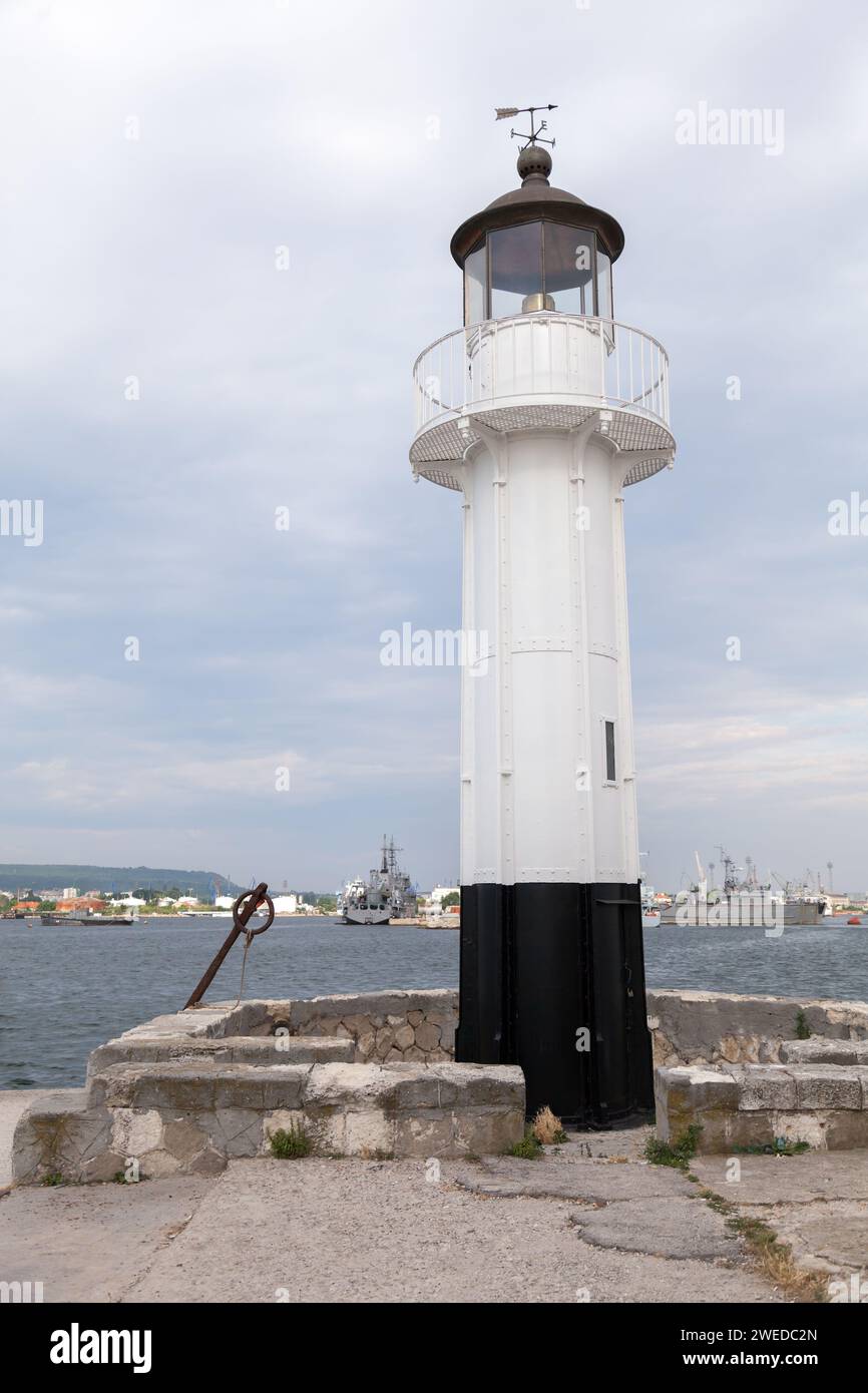 White lighthouse tower with black base is under blue sky on a daytime, vertical photo. Port of Varna, Bulgaria Stock Photo