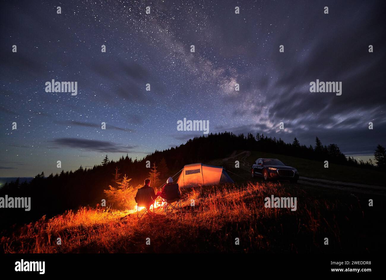 Happy couple staring at starry sky with clouds. Young people sitting in ...