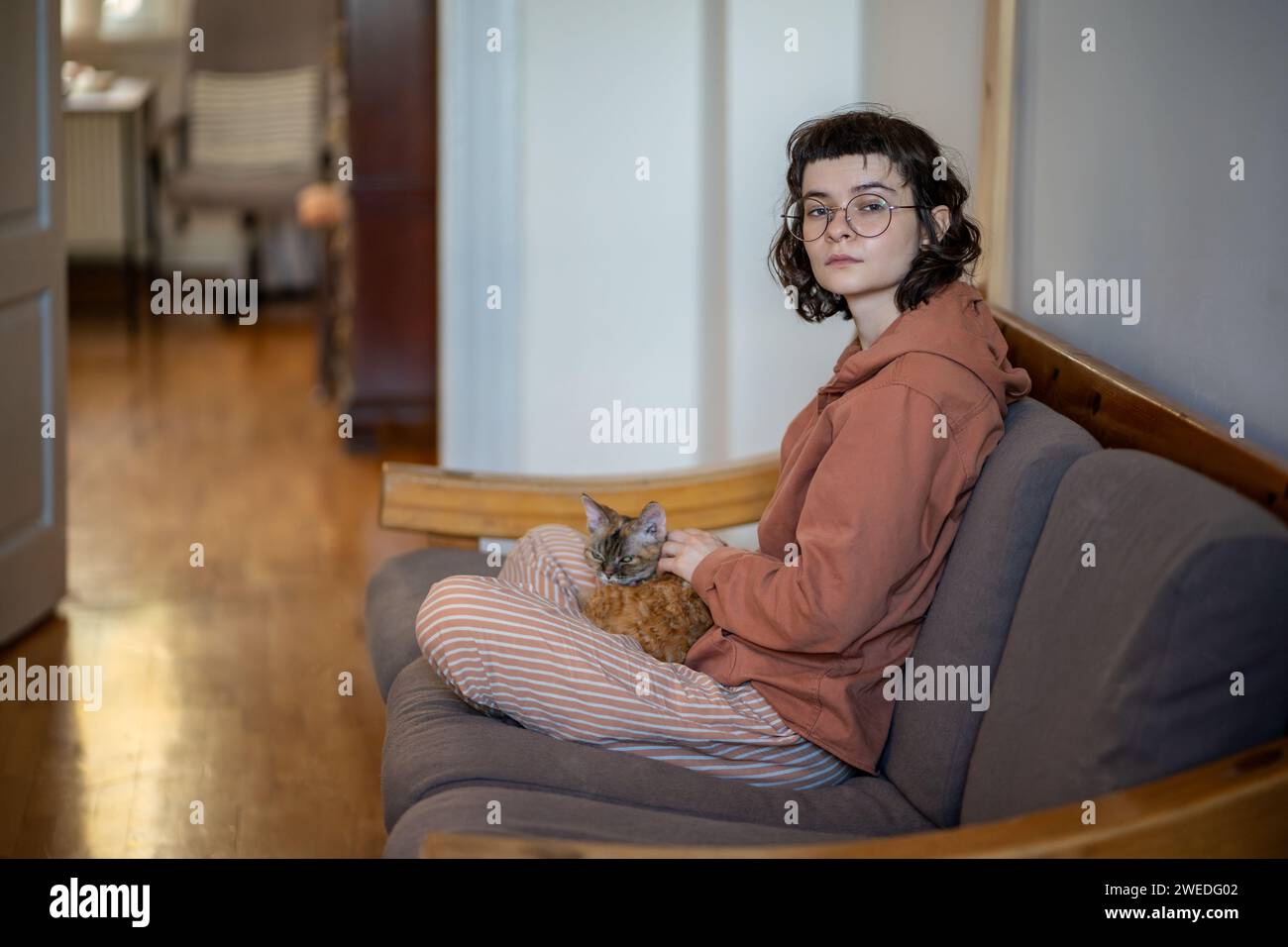 Brooding teenager, pet owner sitting on couch, thinking, stroking sleepy breed cat lying on knees Stock Photo