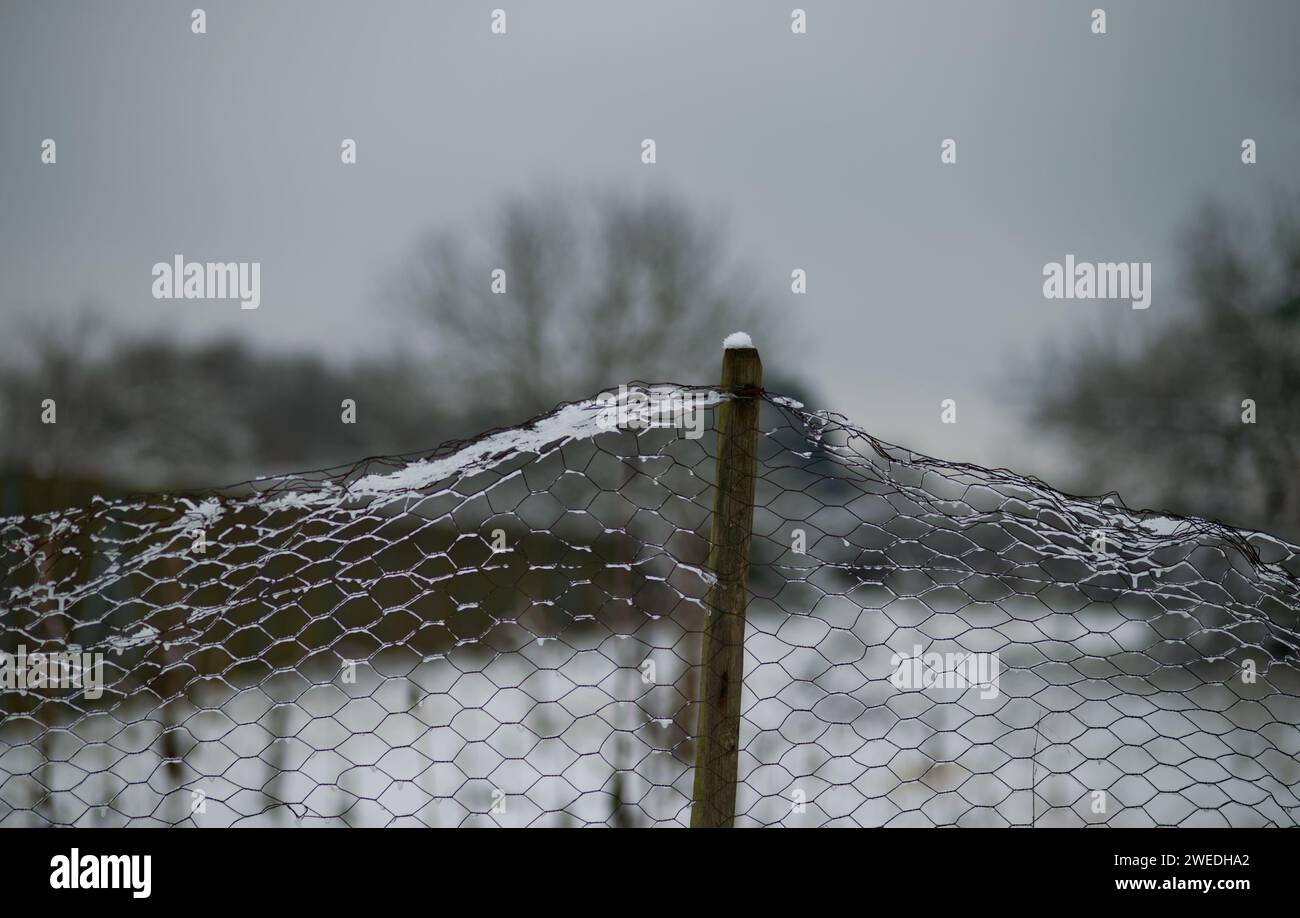 snowcapped wire fence and wooden fencepost in front of a blurred winter scenery at a rural area Stock Photo