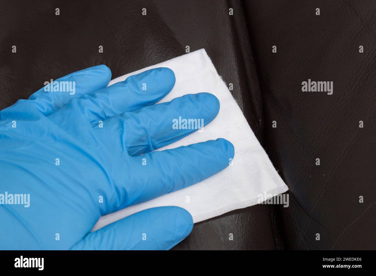 Person cleaning a brown leather sofa couch with a leather cleaner wipe