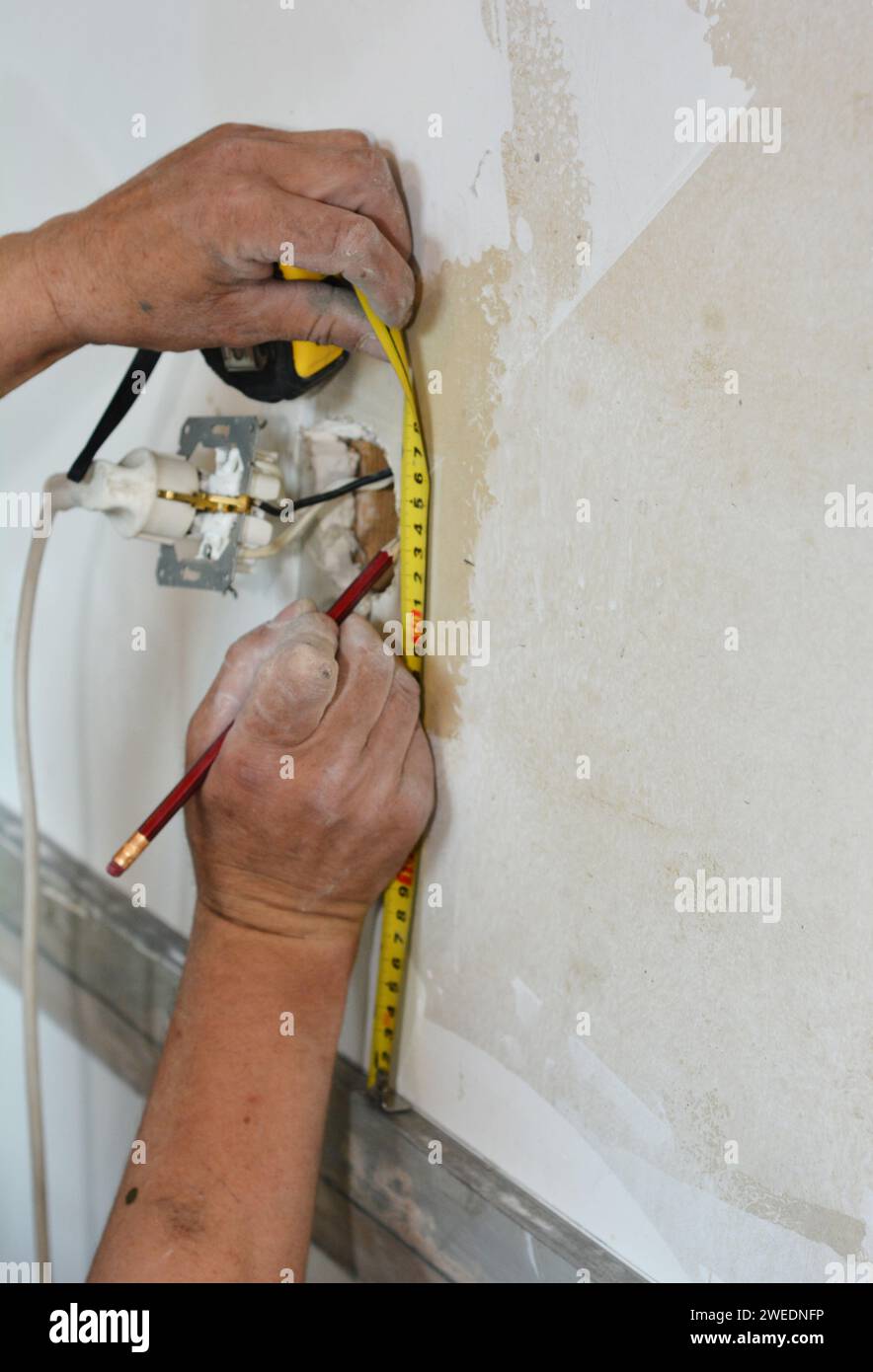 Tiling around electrical outlets over drywall. A man is taking measures carefully to tile around