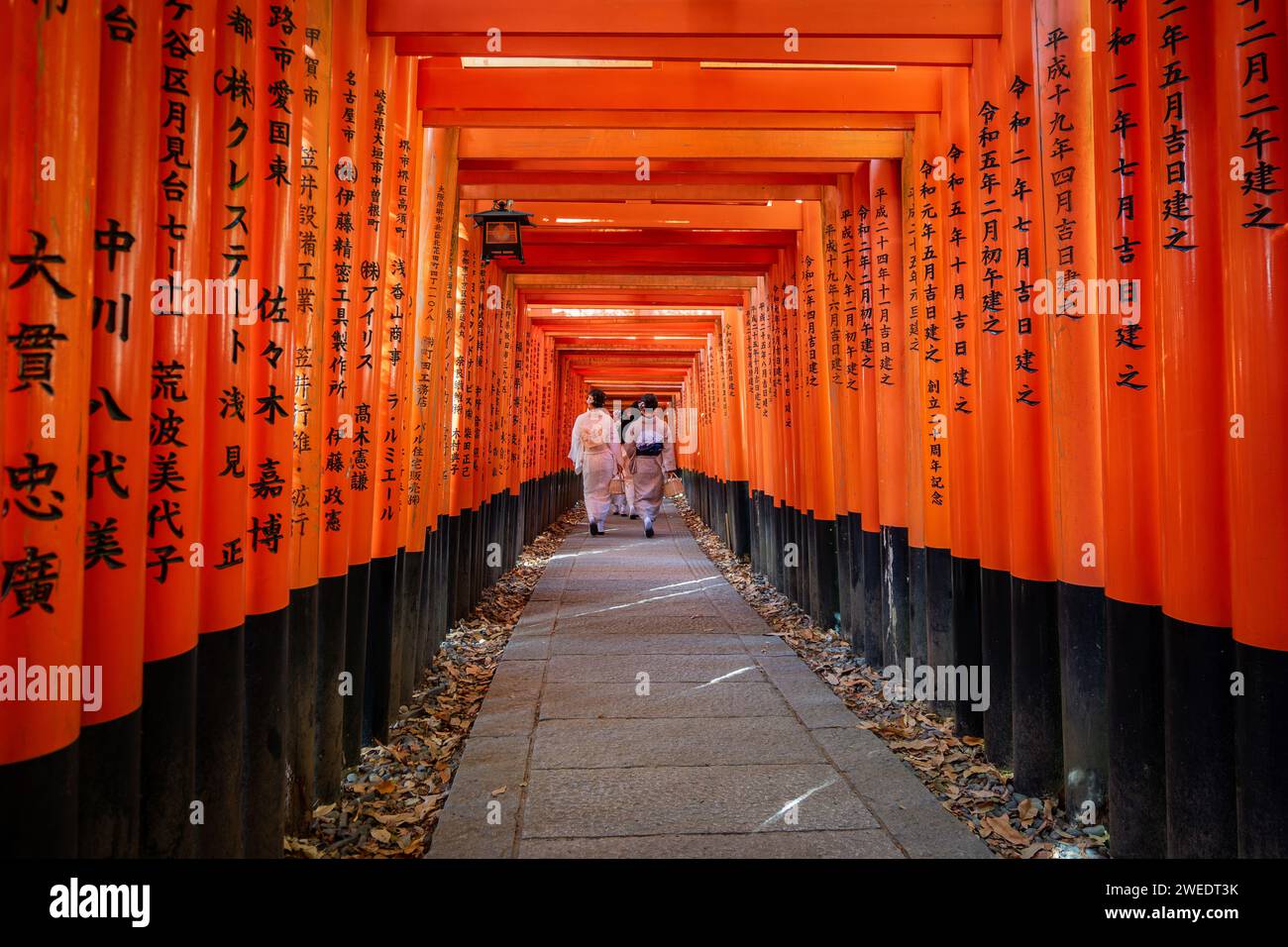 Women in traditional Japanese kimono walking through red torii gates at Fushimi Inari Shrine in Kyoto