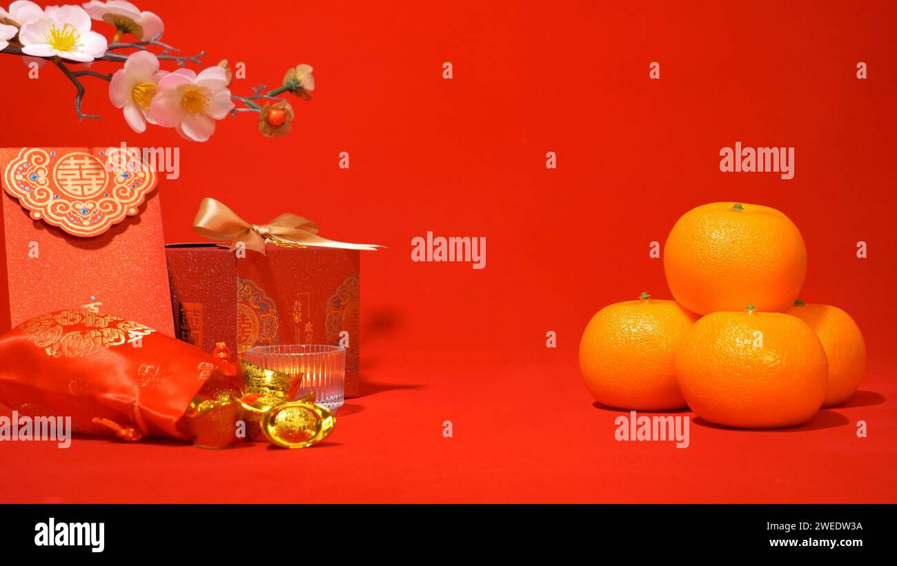 Chinese Lunar New Year background, red theme. gold in silk bag, red gift box with golden bow, red envelope, oranges, plum blossom branch, candle sway Stock Photo