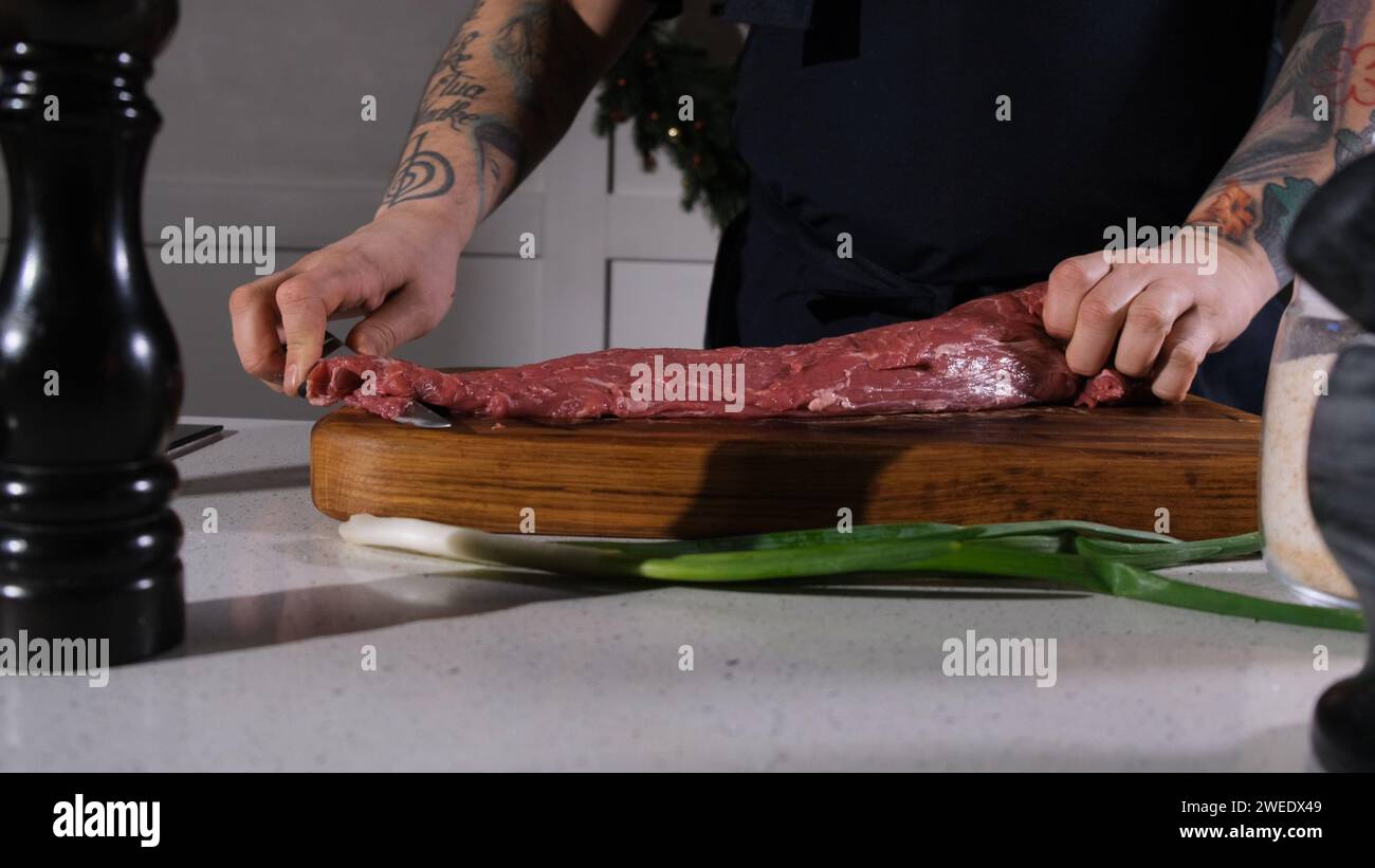 The cook cuts beef meat with a knife on a cutting board. The chef