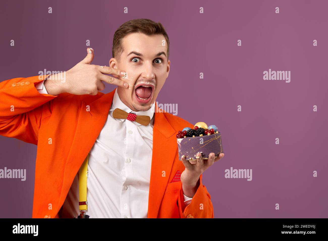 funny man in orange jacket eating cake on purple background Stock Photo ...
