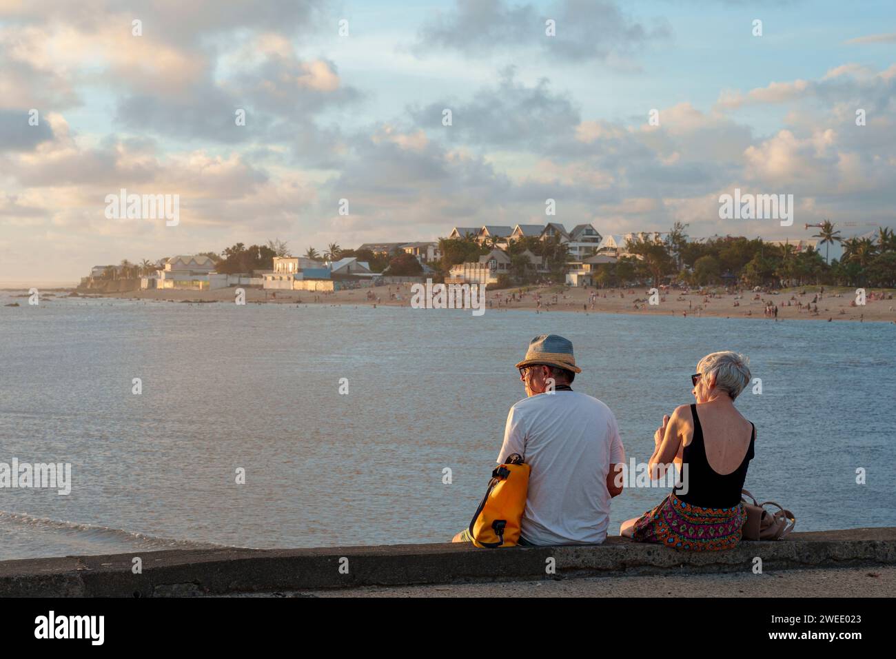A retired tourist couple enjoying the sunset over the lagoon at Saint-Pierre, Réunion Island. They are sitting on the harbour jetty. Stock Photo
