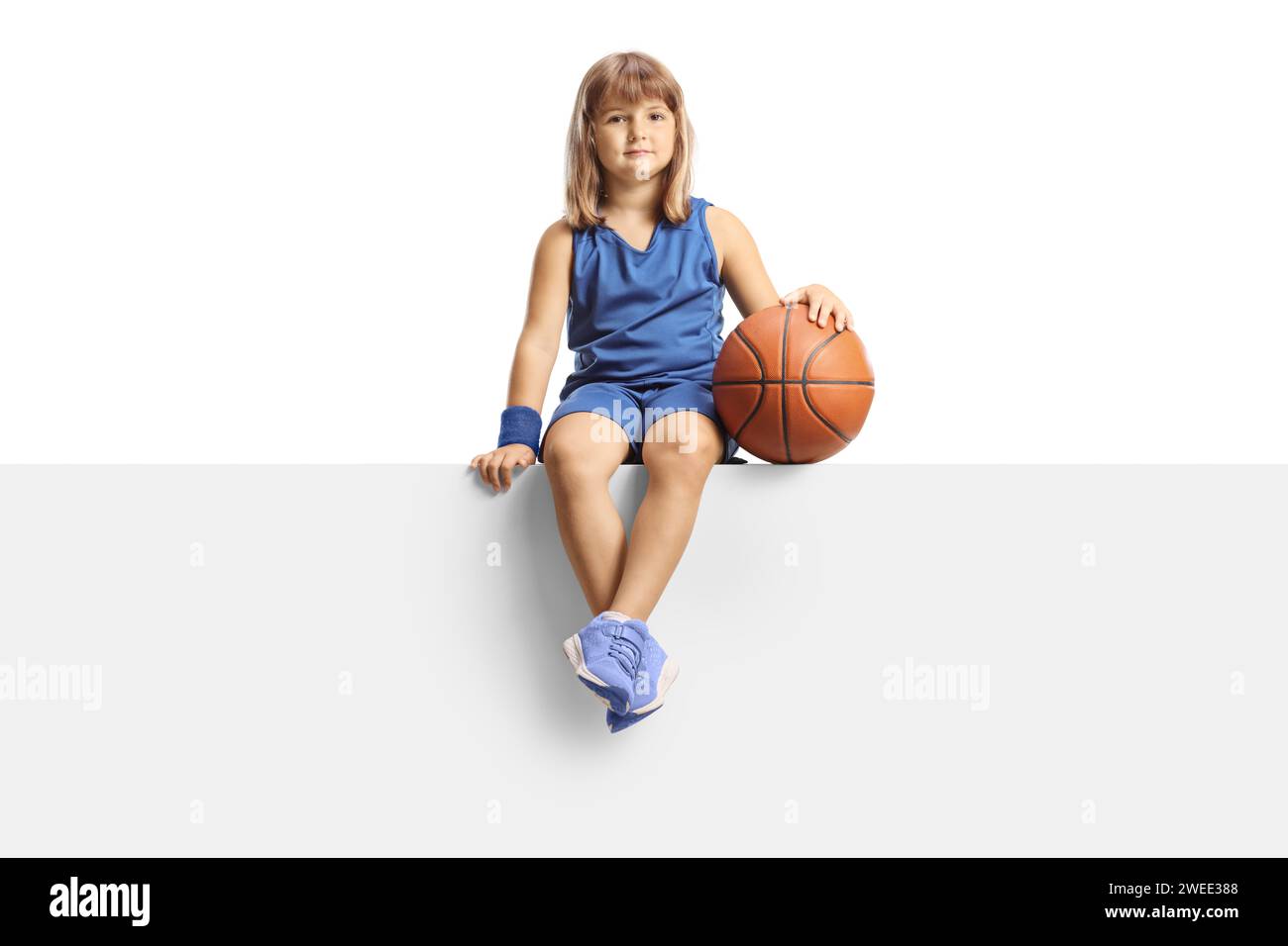 Little girl basketball player sitting on a panel and smiling at camera