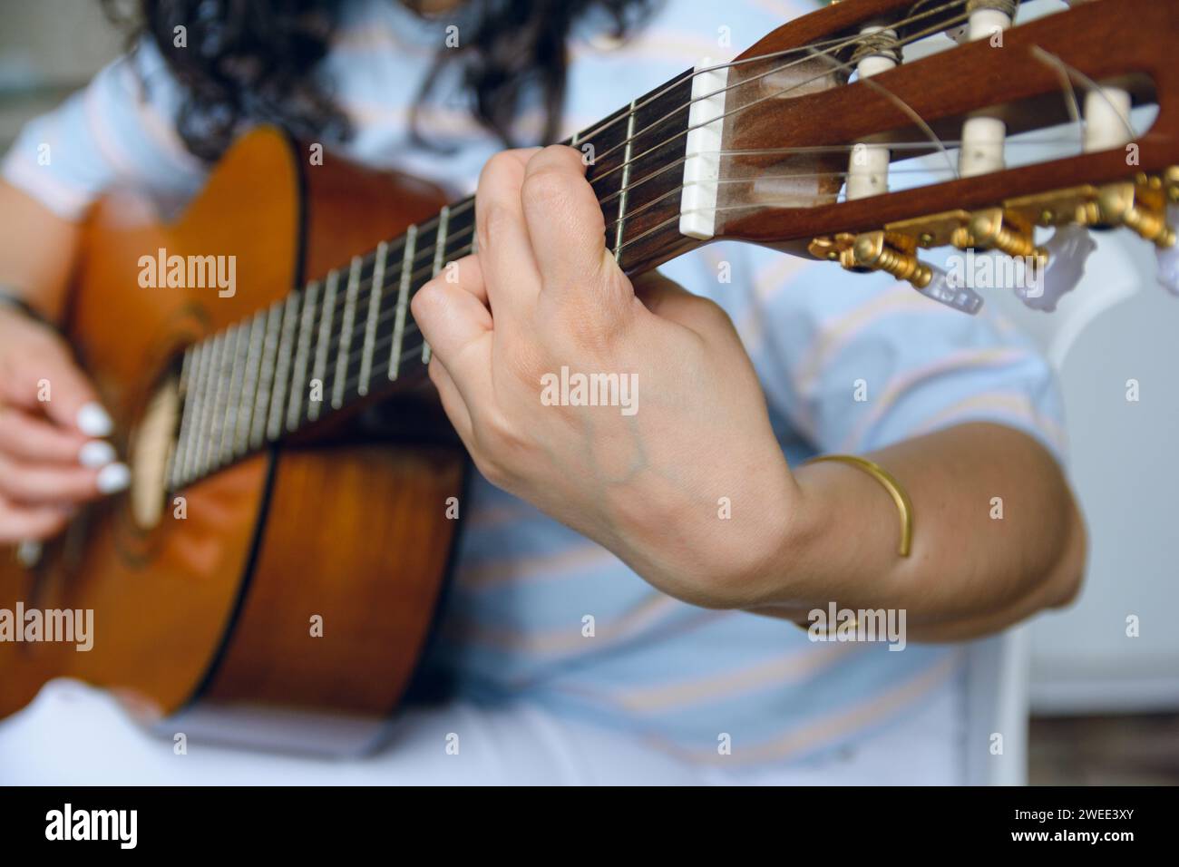 close-up of unrecognizable caucasian woman playing acoustic guitar at home sitting, practicing songs, focus on hand making chord on neck Stock Photo