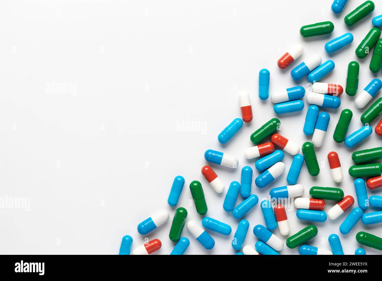 Spilled pills on white background, top view, copy space. Heap of dietary supplements, various colorful vitamins, assorted pharmaceutical medical capsu Stock Photo