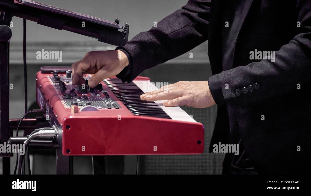 Image of a musician's hand on the keys of a red electrode piano Stock Photo