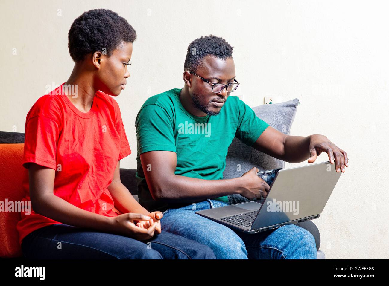 beautiful young african couple sitting together on sofa at home using laptop. Stock Photo