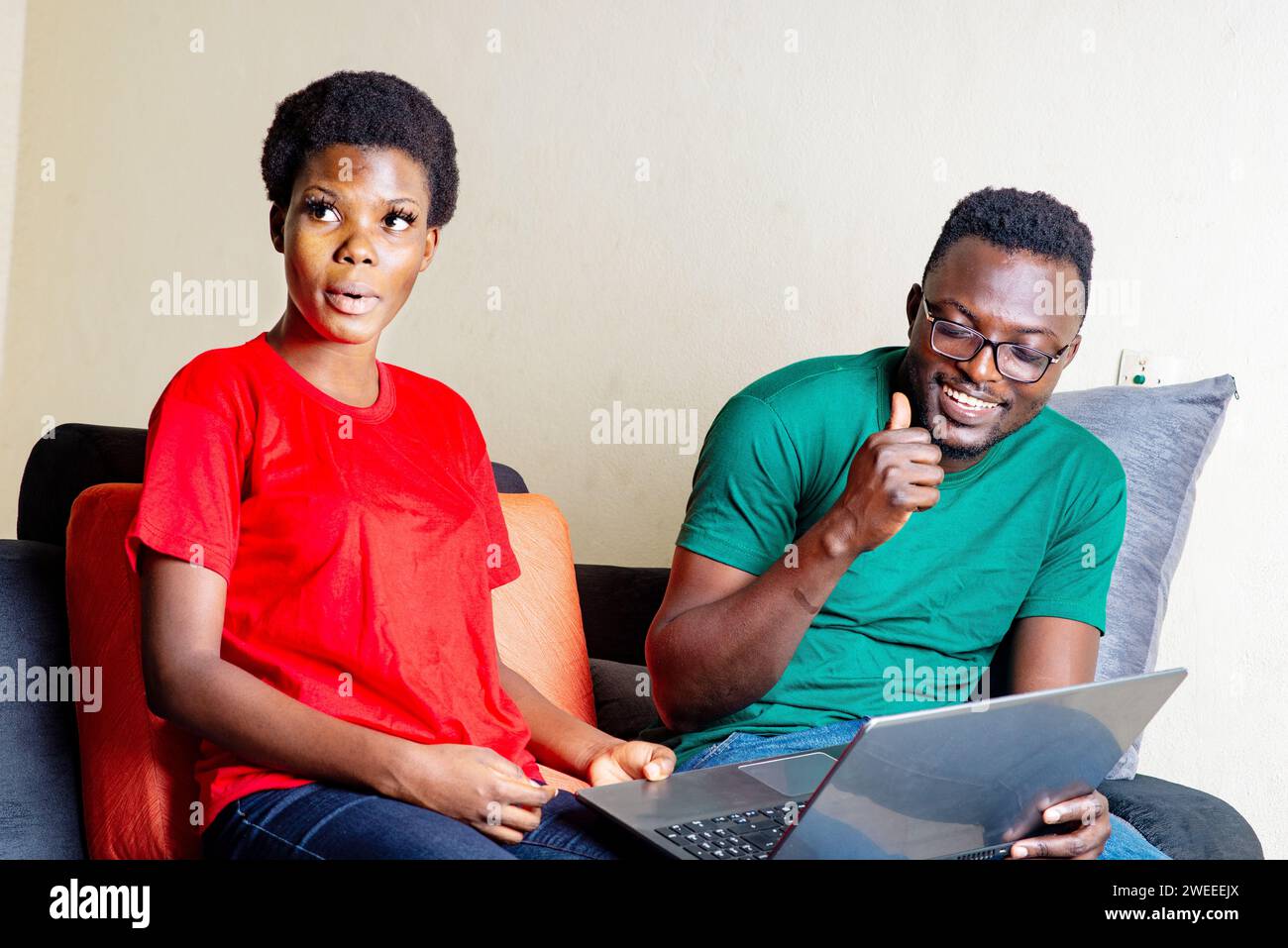 beautiful young african couple sitting together on sofa at home using laptop. Stock Photo