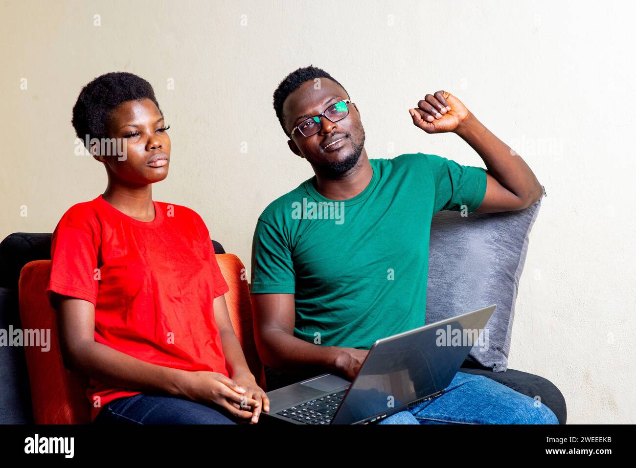 beautiful young couple sitting together on a sofa at home using a laptop. Stock Photo