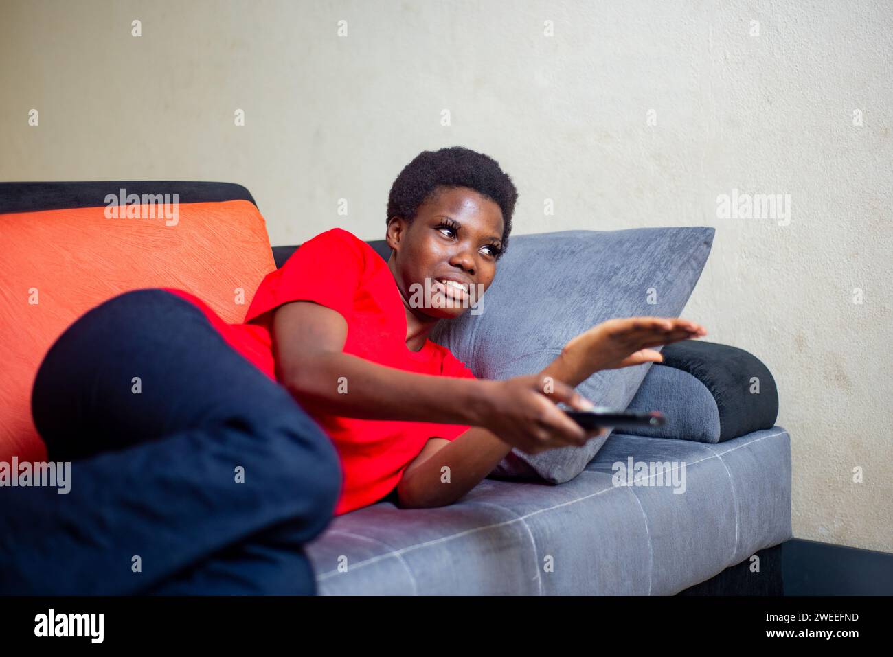 a beautiful young girl lying in a sofa at home holding a remote control looking unhappy. Stock Photo