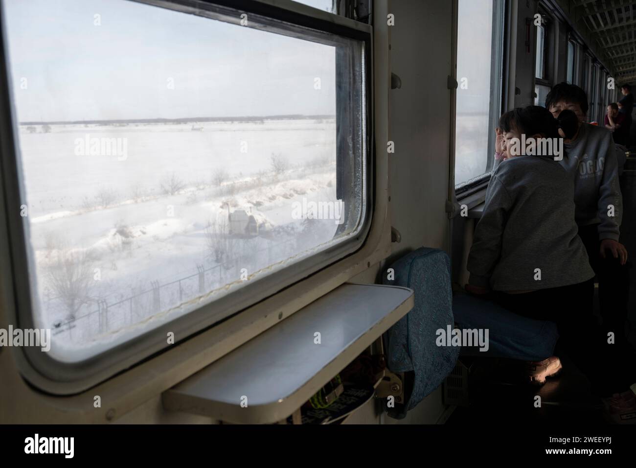 Harbin. 23rd Jan, 2024. Passengers ride the train K7065 from Harbin to Fuyuan in northeast China's Heilongjiang Province, Jan. 23, 2024. The train K7065/K7066 travels to and fro between the city of Harbin and Fuyuan in China's northeastern province of Heilongjiang. With a single journey time of nearly 15 hours, the train replaced old carriages with new ones having air conditioning system, offering a better travel experience for locals who visit friends or commute to work or study along the line. Credit: Cai Yang/Xinhua/Alamy Live News Stock Photo
