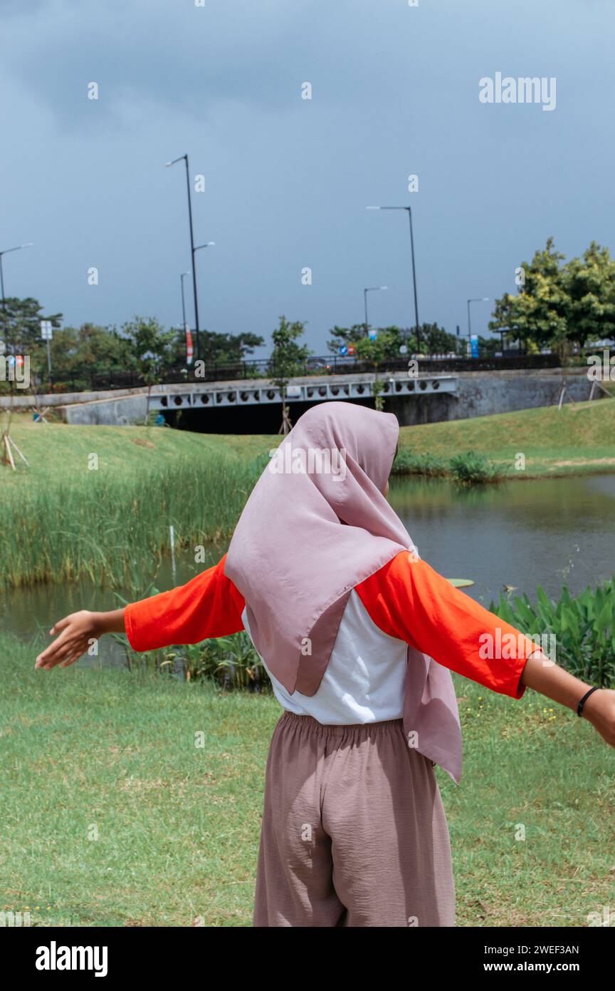 A woman enjoys a serene moment by a river, her colorful attire contrasting the natural backdrop. Stock Photo