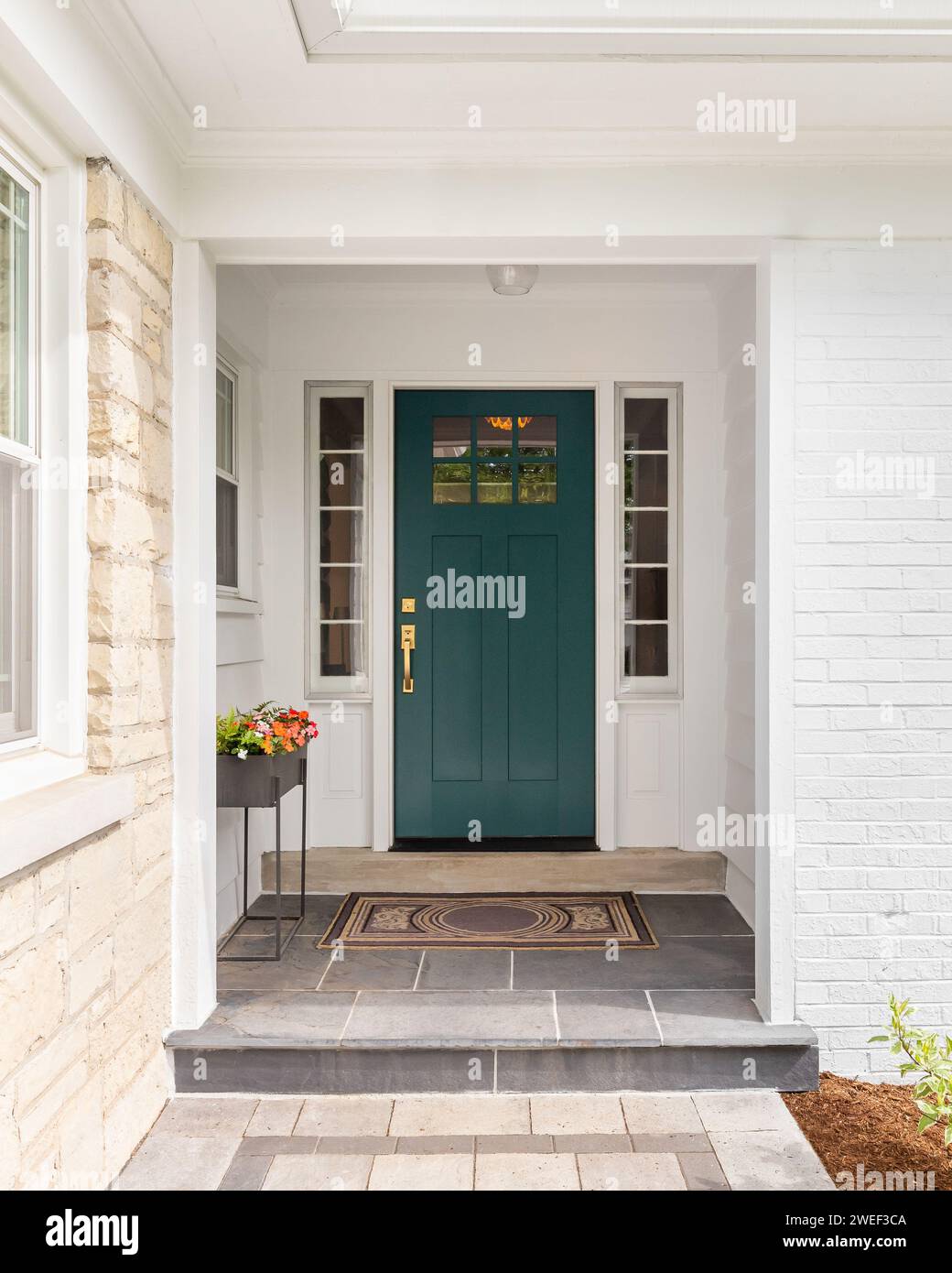 A detail of a front door on home with stone and white brick siding, stone sidewalk, and a colorful blue - green front door. Stock Photo