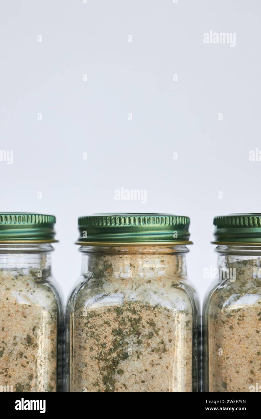 Three jars of garlic, salt and herbs seasoning spices stand close in a row. Glass container with closed green aluminum lid on gray background, recycla Stock Photo