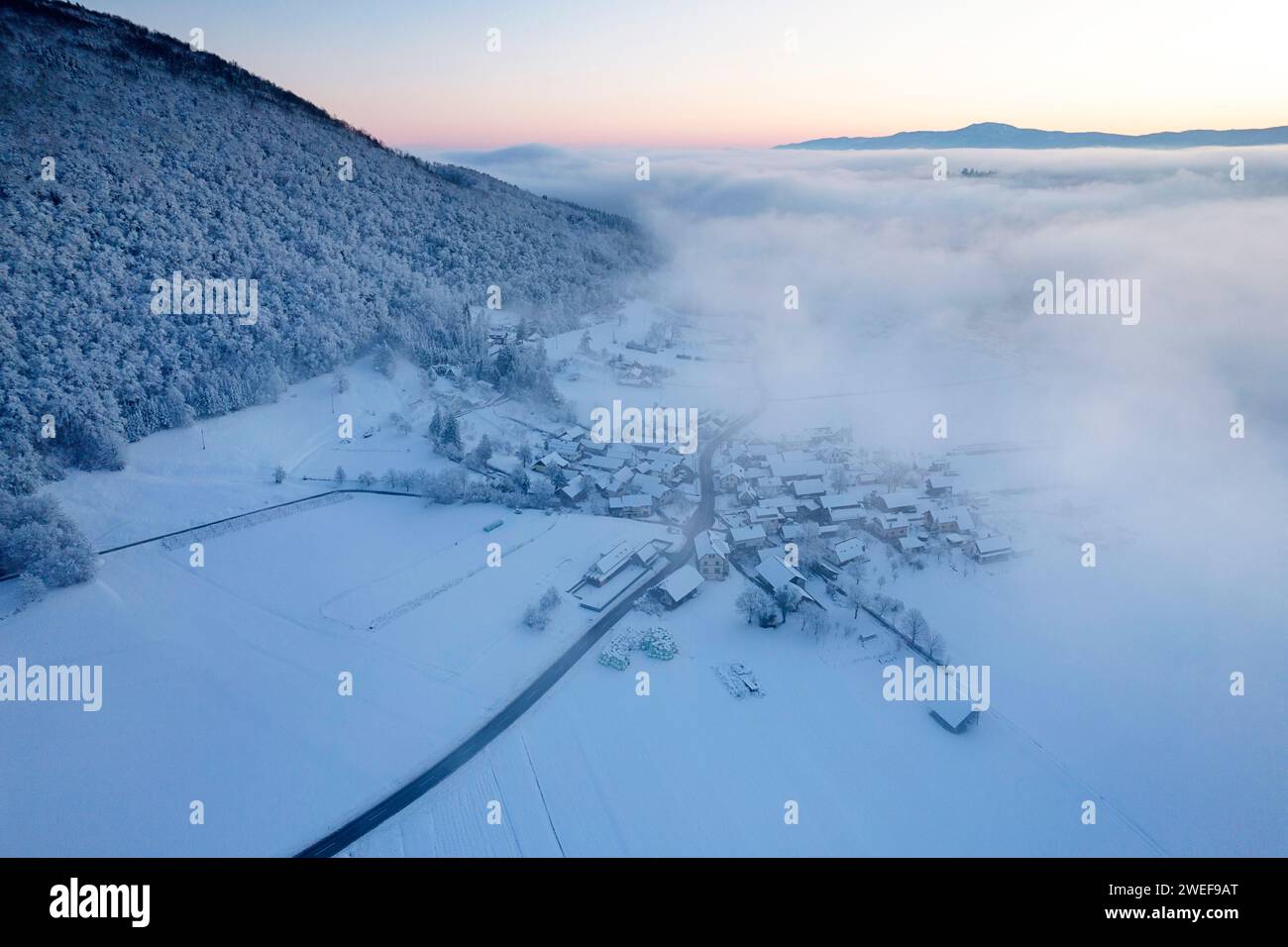 Early morning aerial view towards small village near Dolenjske toplice after heavy snowfall, morning fog still above the valley, Slovenia Stock Photo