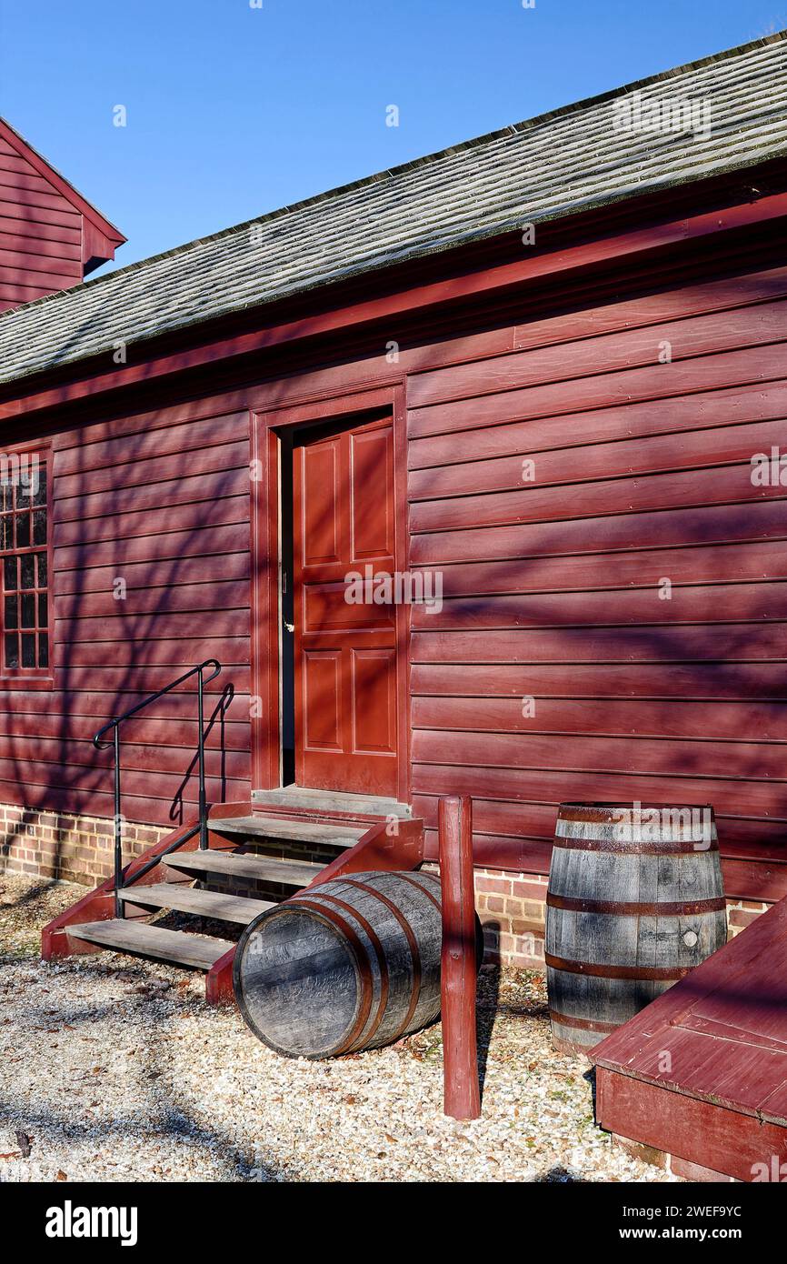 dark red building, plain style, plank steps, 2 wood barrels, wood shingle roof, Colonial Williamsburg; Virginia; Williamsburg; VA Stock Photo