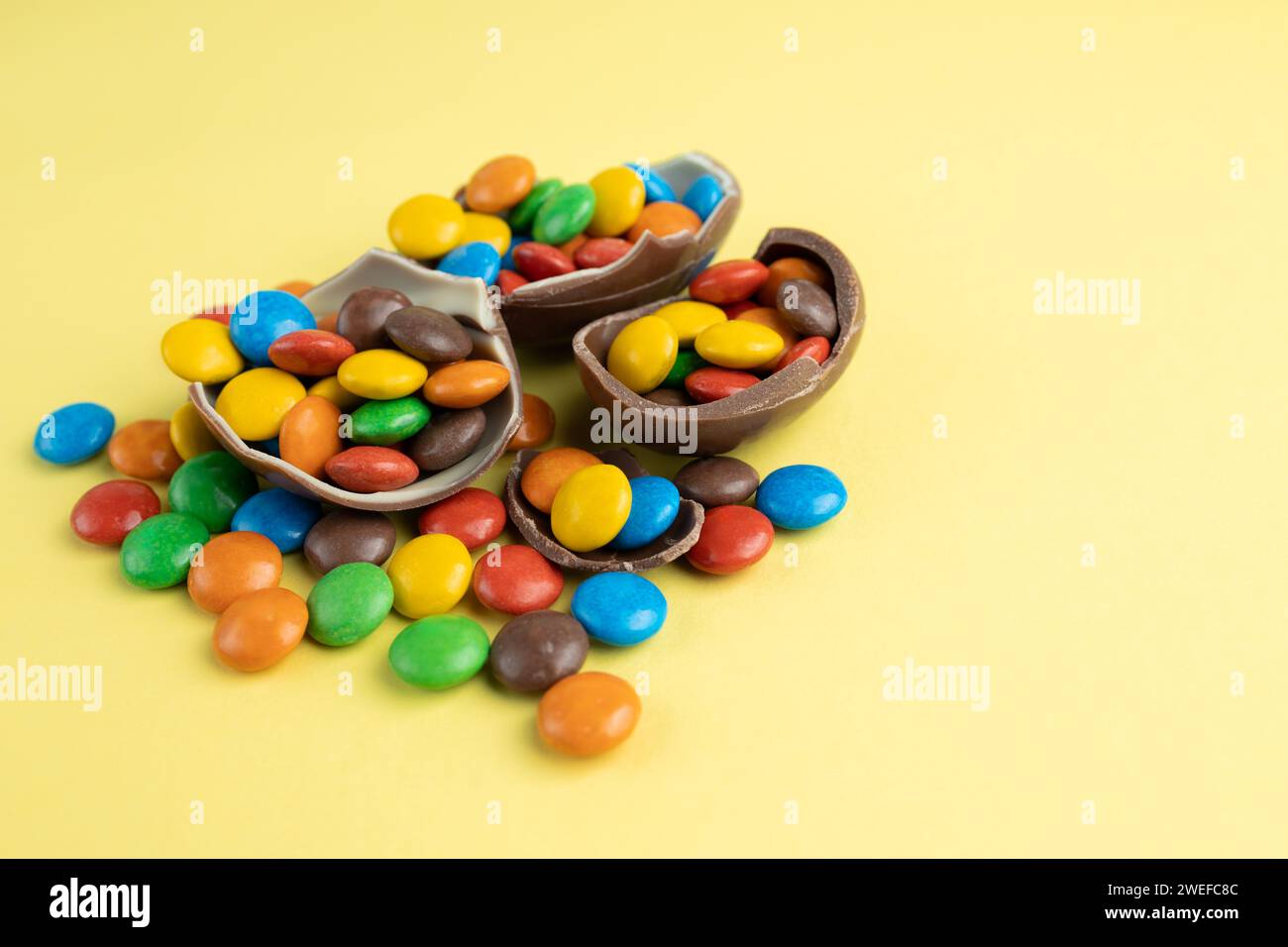 Scattered multi-colored candies in broken Chocolate Easter eggs on yellow background Stock Photo