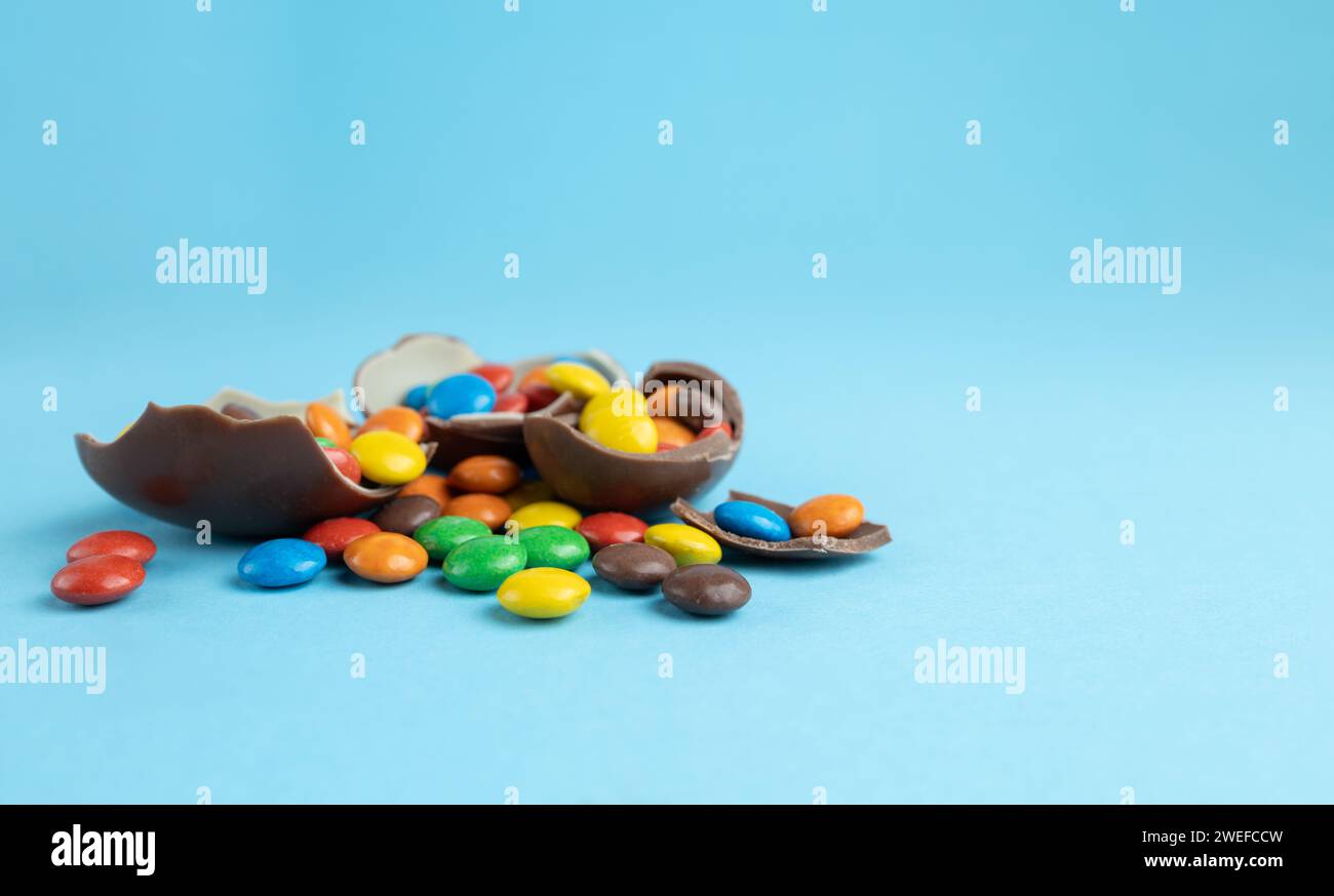 Rainbow candies in broken Chocolate Easter eggs on blue background Stock Photo