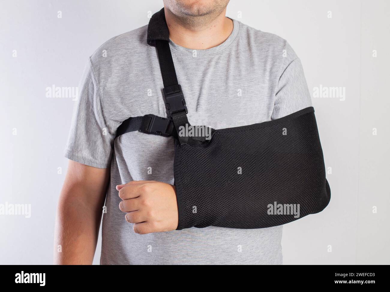 A man on a white background in a bandage to support his arm. Immobilization of the hand and forearm after injury. Rehabilitation after a broken bone. Stock Photo