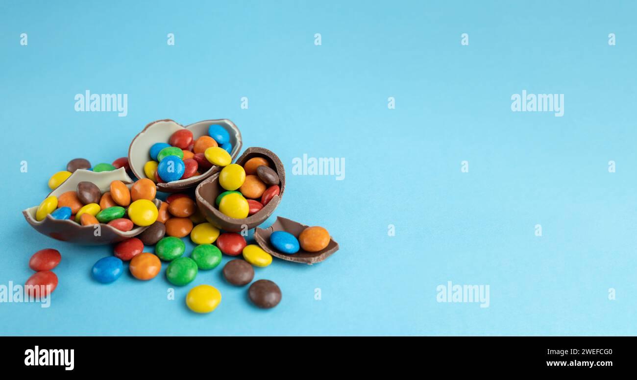 Scattered multi-colored candies in broken Chocolate Easter eggs on blue background Stock Photo