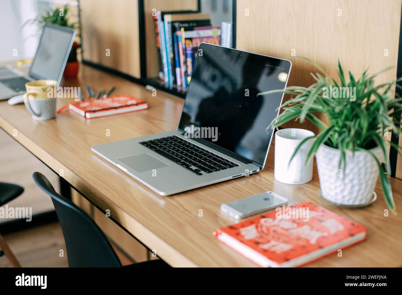 An image of two laptops side by side on a desk in front of a bookcase Stock Photo