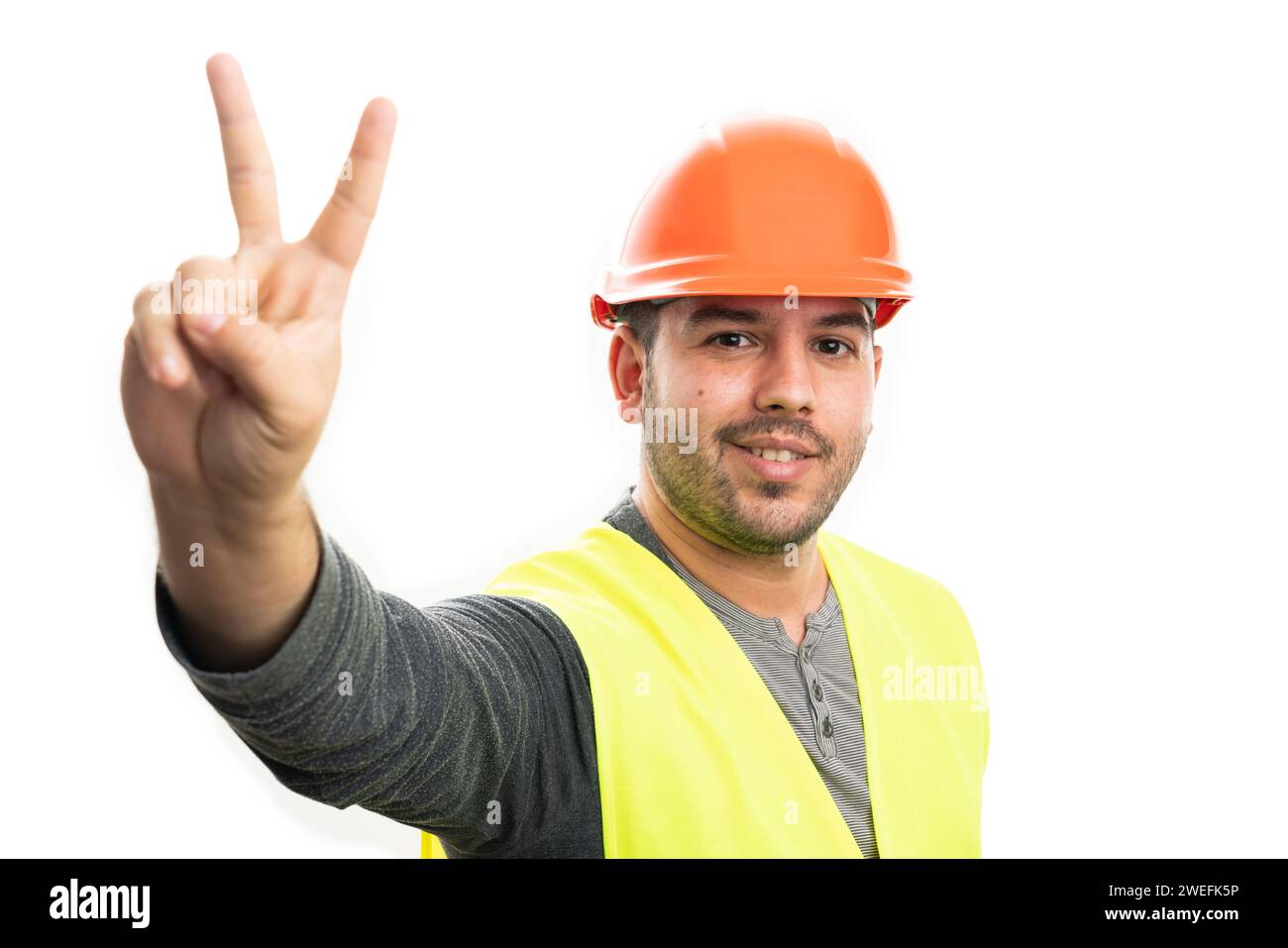 Friendly adult builder man smiling showing peace or victory sign with fingers wearing fluorescent vest and orange hardhat isolated on white studio bac Stock Photo