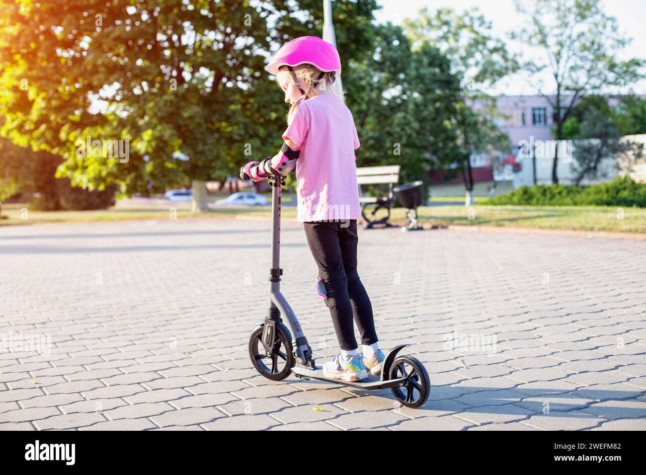 A girl 7 years old in a helmet and a pink injury protection kit rides a ...