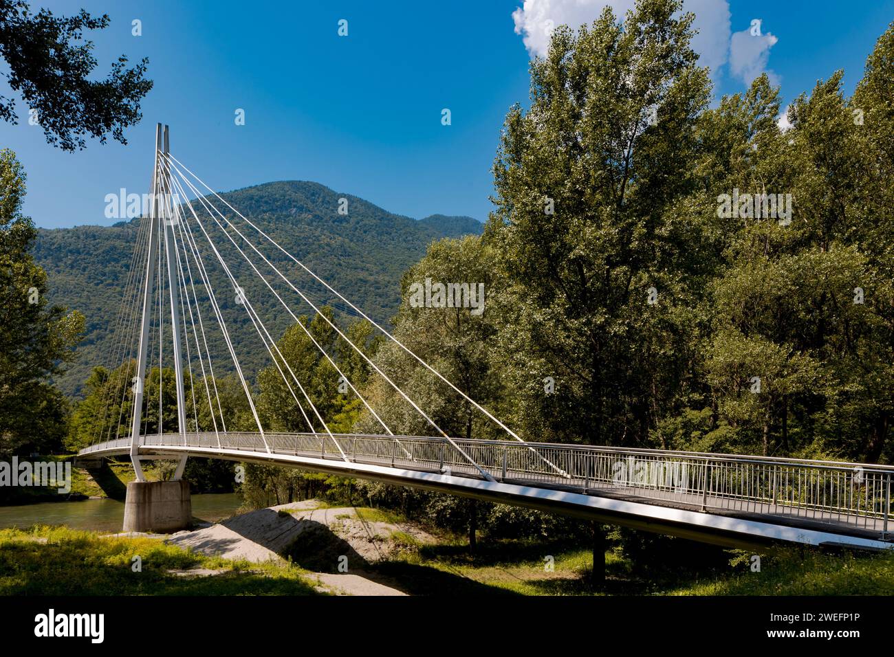 Modern pedestrian bridge in the middle of the mountains of Italian Switzerland, allowing you to cross the Ticino River. Beautiful sunny summer day. Stock Photo