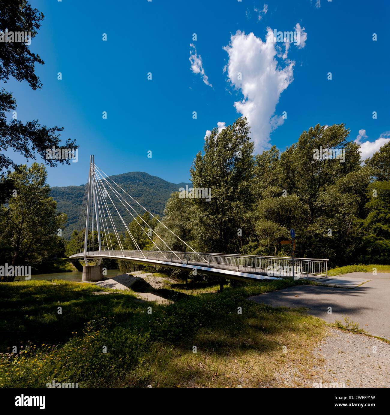Modern pedestrian bridge in the middle of the mountains of Italian Switzerland, allowing you to cross the Ticino River. Beautiful sunny summer day. Stock Photo