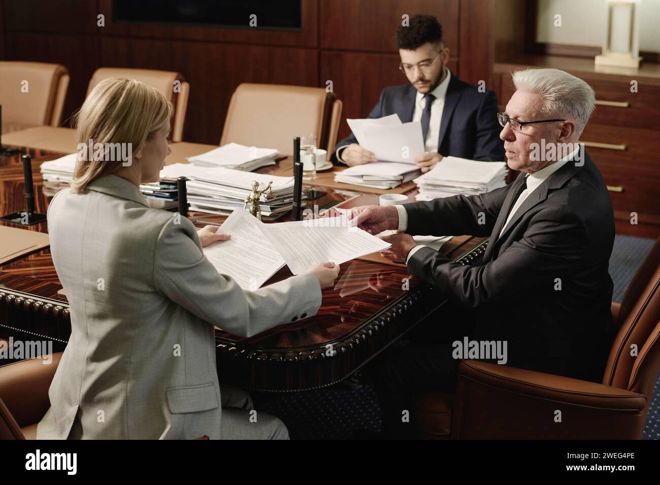 Senior lawyer passing paper to his female colleague, middle eastern man reading papers on background Stock Photo